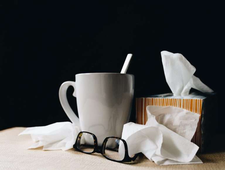 Immagine di una tazza di tisana con accanto una scatola di fazzoletti di carta su sfondo scuro, i rimedi per combattere il raffreddore primaverile