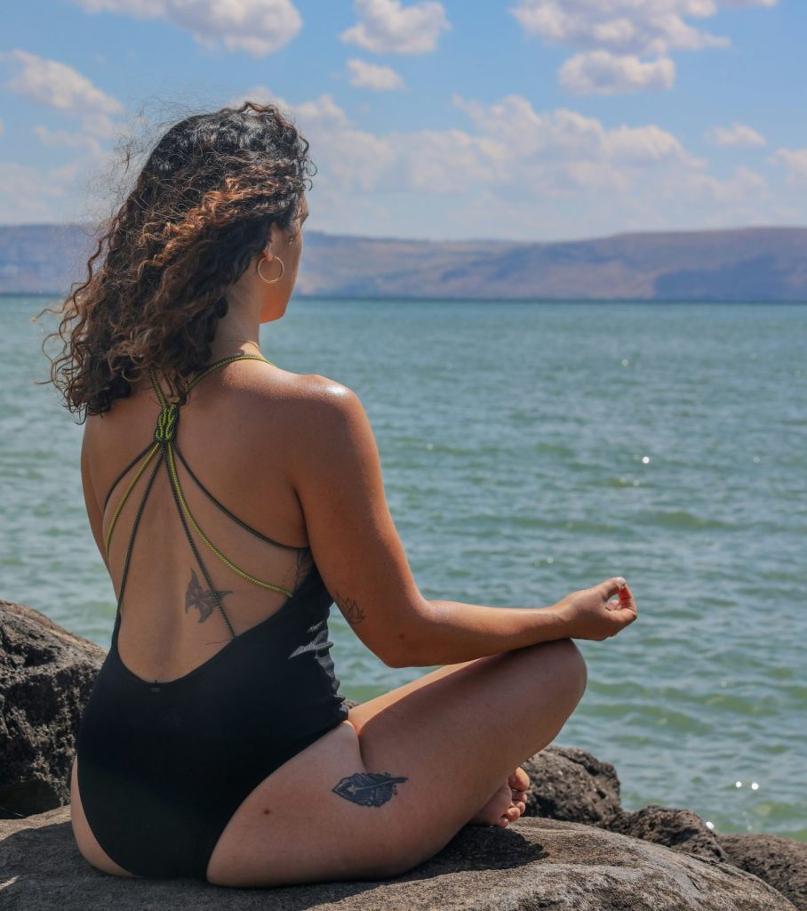 Prepararsi all'estate: donna in costume alle spalle che pratica ginnastica orientale seduta difronte al mare