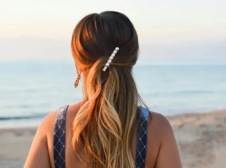 Donna di spalle su una spiaggia all'alba con una magnifica chioma di capelli lunghi biondi. Come preparare i capelli all'estate